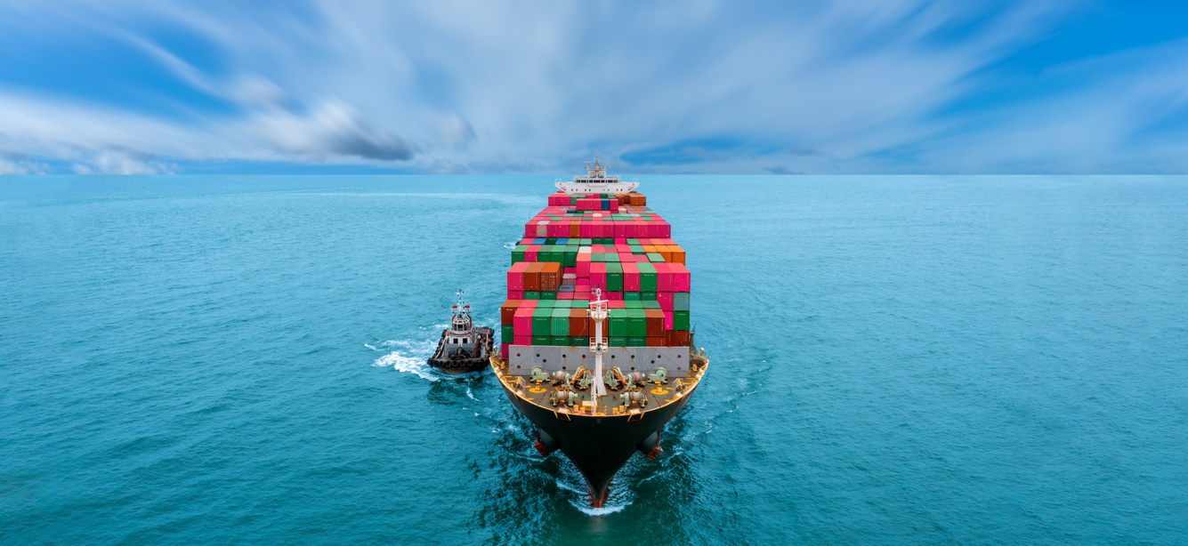 Aerial in front view of cargo ship with contrail in the ocean sea ship carrying container and running for export from container international port to custom ocean concept freight shipping by ship service